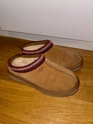 Bruna UGG tofflor med röd kant - Säljer ett par bruna UGG tofflor. Endast använda 4-5 ggr. ❤️