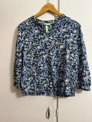 Blommig blus med blå toner - Blus med blommigt mönster i blått, vitt och svart. Modellen har rund halsringning och trekvartsärm med resår vid ärmslut och nederkant. Lätt och luftig känsla, perfekt för en trendig vardagslook.