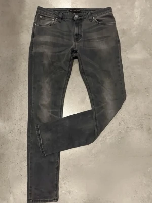 Grå slim fit jeans från Nudie Jeans - Snygga grå slim fit jeans från Nudie Jeans med klassisk femficksmodell och diskreta slitningar framtill. Jeansen har svarta sömmar och Nudie Jeans signaturbroderi på bakfickorna. Tillverkade i mjuk denim med stretch för extra komfort.