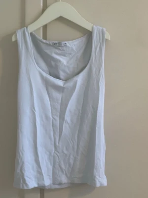 Vit linnetopp från Zara - Säljer en enkel och fräsch vit linnetopp från Zara. Toppen har rundad halsringning och är ärmlös, perfekt för varma dagar eller som layering-piece. Tillverkad i mjuk bomull som känns skön mot huden.