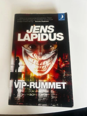 VIP-rummet av Jens Lapidus - Spännande kriminalroman av Jens Lapidus i pocketformat. Omslaget är svart med vita och gula detaljer samt en siluett av en person vid en regnig stadsgata. Boken är på svenska och tillhör genren spänning och deckare.