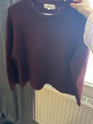 Vinröd stickad tröja från Gina Tricot - Mysig vinröd stickad tröja från Gina Tricot med rund halsringning och lång ärm. Tröjan har en något croppad passform och är gjord i ett mjukt, luddigt material som känns skönt mot huden. Perfekt för lager på lager under kyliga dagar.