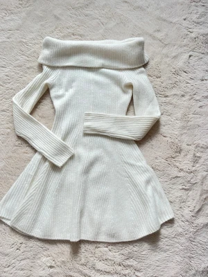 Vit off shoulder stickad klänning - Säljer en vit stickad klänning med off shoulder-ringning och långa ärmar. En fluffig vit accessoar till båda ärmarna ingår.
