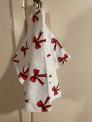 Vit handduk med röda rosetter - Säljer en vit handduk med tryck av röda rosetter över hela tyget. Materialet är mjukt och lätt.