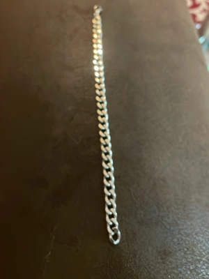 Silverfärgat kedjearmband - Snyggt armband i silverfärg med klassisk kedjedesign. Armbandet har platta, tätt sammanlänkade länkar som ger en stilren och modern look. Perfekt för dig som gillar minimalistiska accessoarer. Materialet ser ut att vara metall. 