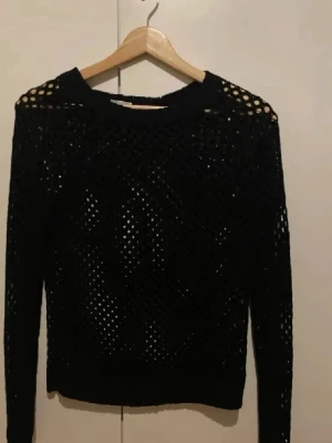 Svart nätstickad tröja - Säljer en svart nätstickad tröja med lång ärm och rund hals. Tröjan har ett genomgående hålmönster som ger en cool och trendig look. Perfekt att styla med ett linne under för en avslappnad vibe.