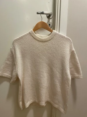 Vit stickad t-shirt från Gina Tricot - Kortärmad stickad t-shirt i mjuk, vit kvalitet från Gina Tricot. Tröjan har rund halsringning med ribbad kant och avslappnad passform. Perfekt att styla lager på lager eller bära som den är för en clean look.