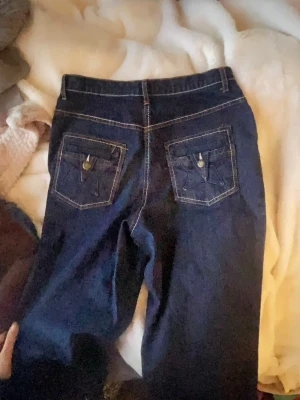 Mörkblå raka jeans med stjärn fickor - Säljer ett par mörkblå jeans med raka ben och snygga bakfickor. Jeansen har klassisk femficksdesign och kontrastsömmar och stjärnor på fickorna, strl 40 ish M/L, brukade använda som baggy, passar ngn under 165cm då kort design. Små små fläckar som knappt syns. Skriv för mer info