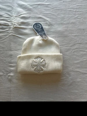 Vit ribbad mössa från Chrome Hearts - Säljer en vit ribbad mössa från Chrome Hearts. Mössan är tillverkad i mjukt stickat material och har en uppvikt kant. Perfekt för dig som vill ha en clean och stilren look. Helt ny aldrig använd