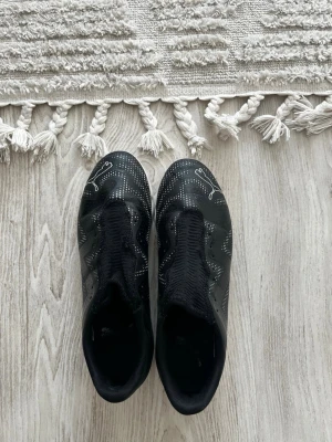 Svarta Puma fotbollsskor - Säljer ett par svarta inomhus fotbollsskor från Puma med vit logga på hälen och diskreta vita detaljer på ovandelen. en tight och modern passform. Perfekta för dig som vill ha stilrena och funktionella skor på planen, snöre medföljer.