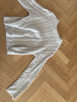 Ljusrosa kabelstickad tröja - Mysig ljusrosa kabelstickad tröja med rund hals och långa ärmar. Tröjan har ett klassiskt flätmönster framtill och på ärmarna samt ribbade muddar vid ärmslut och nederkant. Perfekt för lager på lager och en avslappnad stil.