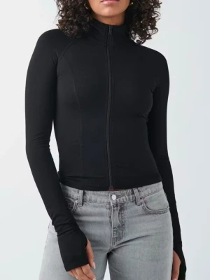 Svart ziptröja med tumhål - Slimmad svart ziptröja med hög krage och långa ärmar med tumhål. Tröjan har en minimalistisk design utan synligt märke och är gjord i ett stretchigt, mjukt material som sitter tajt mot kroppen. Perfekt för en clean och sportig look. Stl M men passar S!!