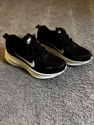 Nike Vomero 18, löparskor  - Helt nya och oanvända skor. Nypris: 1749kr. Snygga svarta sneakers från Nike med vit sula och klassisk vit swoosh på sidan. Ovandelen är i mesh för bra andningsförmåga och skorna har svarta skosnören. Perfekta för dig som gillar sportig stil och vill ha bekväma skor till vardagen.