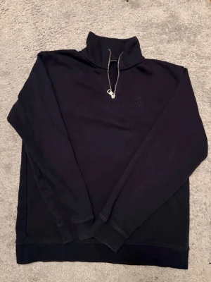 Svart halfzip hoodie med hög krage - Svart hoodie från Peak Performance med halfzip och hög krage. Tillverkad i mjukt bomullsmaterial och har diskret logga broderad på bröstet. Klassisk och stilren design med långa ärmar och ribbade muddar.