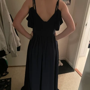 Mörkblå balklänning med volang - Elegant mörkblå balklänning med smala axelband och djup v-ringning både fram och bak. Klänningen har volangdetaljer vid bysten och ett fint fall. Perfekt för speciella tillfällen.Min yngsta poserar men denna klänning för stor för henne men bara för å visa den på.Från bubbleroom.