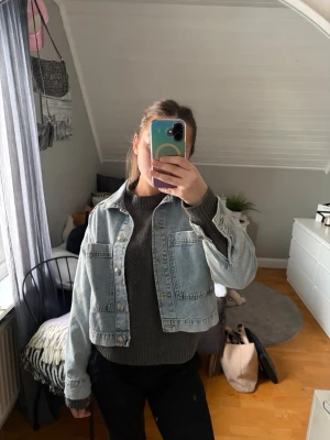 Ljusblå cropped jeansjacka - Säljer en ljusblå jeansjacka med klassisk knappstängning och två stora bröstfickor. Jackan är cropped och har en avslappnad passform, perfekt att slänga över en tröja. Enkel och stilren design som funkar till många outfits.