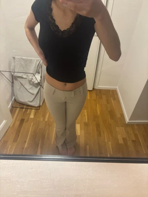 Beige kostymbyxor med låg midja - Snygga beige kostymbyxor med låg midja och raka ben. Byxorna har bälteshällor och en enkel design utan synliga fickor framtill. Perfekta för en clean och stilren look.