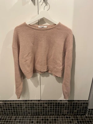 Ljusrosa cropped stickad tröja från NA-KD - Säljer en ljusrosa cropped stickad tröja från NA-KD. Tröjan har rund halsringning, långa ärmar och ribbade muddar vid ärmslut och nederkant. Perfekt till höst och vinter för en avslappnad och trendig look.