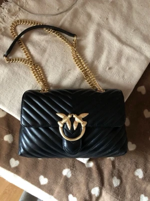 Svart handväska - Säljer en svart quiltad handväska Pinko med guldfärgad kedjerem och ikoniskt fågelspänne framtill. 