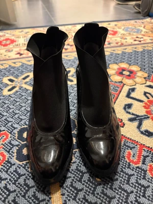 Ett par fina klack skor - Säljer ett par svarta pumps i glansigt lackmaterial med en cool, vågig kant upptill. Skorna har rundad tå och bred klack som ger stabilitet. De har en modern och edgy look som sticker ut. Perfekta för dig som vill ha något annorlunda i skogarderoben.