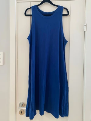 Blå ärmlös klänning i bomull - En enkel och snygg blå klänning i mjuk bomull. Klänningen är ärmlös med rund halsringning och har en lös passform som ger en avslappnad look. Perfekt för varma dagar och lätt att styla med accessoarer. Trikåklänning armlös mörkblå strl XL.  Lite nopprig på några ställen i övrigt i bra begagnat skick   Mått Över bröstet: ca 53 cm Längd från axeln och ner: ca 104 cm  95% rayon och 5% spandex  Kommer från ett djur och rökfritt hem