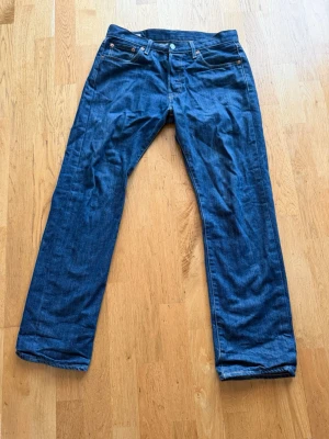 Blå raka jeans i klassisk modell - Säljer ett par blå jeans med rak passform och fem fickor. Jeansen har klassisk denimlook med kontrastsömmar och knappgylf. Perfekta för dig som gillar enkel och tidlös stil.