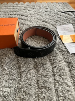 Svart bälte  - Snyggt svart bälte med klassiskt monogrammönster och matt svart spänne. Insidan är brun och bältet har en stilren design som passar till många outfits. 