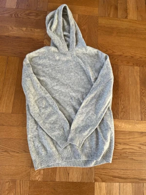 Grå stickad kashmir hoodie  - Säljer den här tvärfeta stickade grå kashmir hoodien. Snörerna vid luvan är borttagna då dom var rätt långa och de flesta föredrar utan snören Tröjan har inga lappar eller broderingar eller liknande så märket är okänt.Oavsett är tröjan av väldigt hög kvalitet, jätteskön passform och snygg design. Tröjan är tillverkad med 50% kashmir och 50%ullblandning. Uppskattad storlek: S/M Toppskick, inga defekter alls.