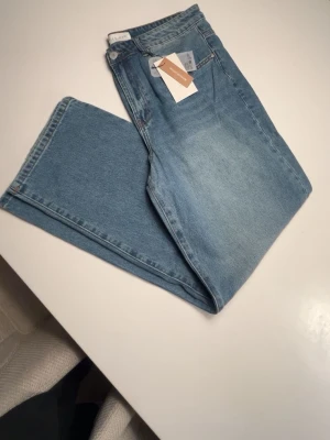 Ljusblå raka jeans från Pier One - Säljer ett par ljusblå jeans från Pier One med rak passform och klassisk femficksdesign. Jeansen har hög midja och är tillverkade i ett mjukt denimtyg. Perfekta för en avslappnad och trendig look.
