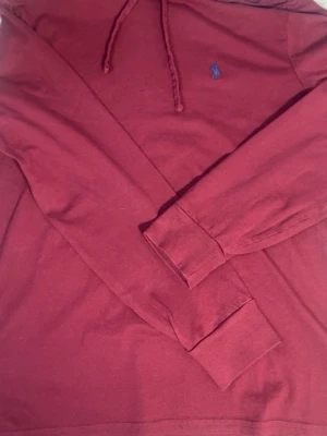 Vinröd hoodie från Polo Ralph Lauren - Snygg vinröd hoodie från Polo Ralph Lauren med klassisk huva och dragsko. Tillverkad i mjukt bomullsmaterial och har den ikoniska blå loggan broderad på bröstet. Perfekt för en chill och stilren look.