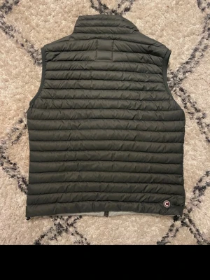 Mörkgrön dunväst från Colmar - Snygg mörkgrå dunväst från Colmar med quiltad design och två dragkedjefickor framtill. Västen har hög krage och Colmar-logga på bröstet. Perfekt för lager-på-lager och håller dig varm utan att bli för tung. Materialet är lätt och smidigt.  Den är storlek 50 i ”colmar” storlek
