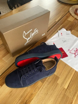 Mörkblå mockasneakers Louboutin - Mörkblå sneakers från Christian Louboutin i mjuk mocka med ikonisk röd sula. Helt nya loubs aldrig använda 10/10 skick. Flera storlekar 43,44,45. Allt OG medföljer tillbehör. OBS tar slut snabbt!! Pris kan diskuteras vid snabb affär 