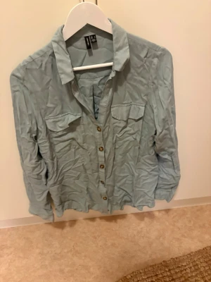 Ljusblå skjorta från H&M - Ljusblå skjorta från H&M med klassisk krage, två bröstfickor och knappar framtill. Skjortan har lång ärm och är tillverkad i ett mjukt material som känns skönt mot huden. Perfekt att styla till jeans eller kjol.