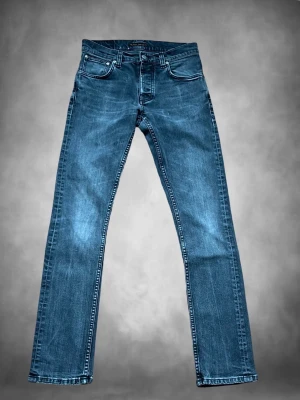 Blå raka jeans från Nudie Jeans - Säljer ett par klassiska blå jeans från Nudie Jeans med rak passform och fem fickor. Jeansen har snygga kontrastsömmar och är tillverkade i slitstark denim. Perfekta för dig som gillar en tidlös och enkel stil.