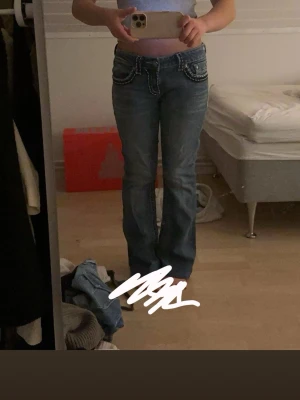 Blå bootcut jeans ifrån miss me - Säljer ett par blå bootcut jeans ifrån miss me med vita kontrastsömmar och dekorativa fickor bak. Jag har köpt dom för 850 spänn i en second hand butik. Dom e för stora därför säljer jag. Jeansen har låg midja och detaljerade knappar samt ficklock. Perfekta för dig som gillar en avslappnad men ändå snygg stil.