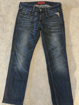 Replay anbass  - Snygga blå jeans från Replay med raka ben och klassisk femficksmodell. Jeansen har slitningar och ljusare partier framtill för en cool, använd look. Tydliga kontrastsömmar och Replay-logga på fickan. Perfekta till en avslappnad stil.