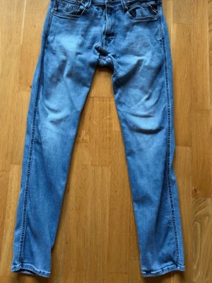 Ljusblå slim fit replay jeans - Säljer ett par ljusblå skinny jeans med klassisk femficksdesign och diskreta sömmar på bakfickorna. Jeansen har en smal passform och är tillverkade i mjukt denimtyg som ger en avslappnad look. Perfekta till sneakers eller boots.