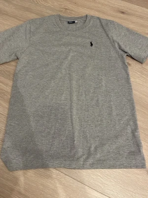 T-shirt - Snygg grå t-shirt från Polo Ralph Lauren med klassisk passform och rund hals. T-shirten har det ikoniska lilla Polo-logotrycket på bröstet och är gjord i mjukt bomullsmaterial. Perfekt basplagg till garderoben.