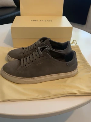  Axel Arigato, clean 90 suede - Snygga grå sneakers från Axel Arigato med låg profil och platt vit sula. Skorna har rund tå, snörning och är tillverkade i mocka med detaljer i skinn på hälen. Perfekt för dig som gillar stilrena sneakers.  Skorna tillkommer med box och dustbag, samt påsen om man vill göra meetup. Skorna har tecken på användning, mockan har fått sämre kvalité, dessutom har den ena skon fått en skvätt färg vilket sänker värdet . Nypris: 2700kr. Pris kan diskuteras! 