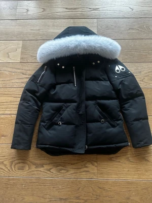 Svart dunjacka med pälskant Moose Knuckles - Helt ny och snygg svart dunjacka från Moose Knuckles med stor huva och lyxig vit pälskant. Jackan har två bröstfickor med dragkedja, två snedställda fickor fram och logga på ärmen. Insidan är fodrad och jackan har en klassisk puffad look. Pris kan diskuteras via dm vid snabbt köp!!!