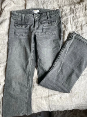 Grå jeans från Gina Tricot - Snygga grå jeans från Gina Tricot med bootcut design och två framfickor med lock och knapp. Klassisk femficksmodell i mjukt denimtyg, perfekta till en avslappnad stil. Passar dig som gillar enkel och stilren look. Skriv om ni har andra frågor!🥰