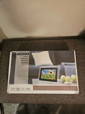 7-tums digital fotoram nytt I förpackning  - Digital fotoram med 7-tums skärm. Kommer i originalkartong med fjärrkontroll och strömkabel. Perfekt för att visa dina favoritbilder i ett modernt format. Fotoramen är svart och silverfärgad och har stöd för JPEG-format.