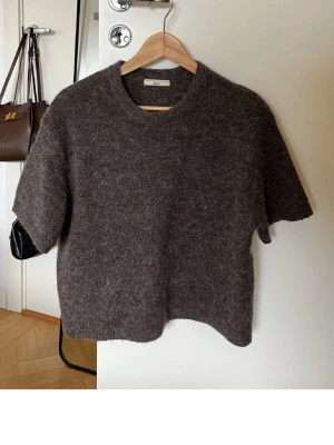 Brun stickad t-shirt från Totême - Mysig brun stickad t-shirt från Totême i mjuk ullmix. Tröjan har korta ärmar, rund halsringning och en rak, avslappnad passform. Perfekt för lager på lager och en stilren vardagslook.