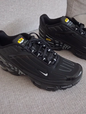 Nike Air Max Plus Tn svarta sneakers - Snygga svarta Nike Air Max Plus Tn sneakers med Tuned Air-dämpning. Skorna har en sportig design med svarta och grå detaljer, mesh och syntetmaterial samt små vita Swoosh-loggor på sidan. Perfekta för dig som gillar streetwear och vill ha en modern look.