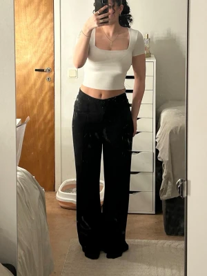 Vit croppad topp med fyrkantig hals - Säljer ett par svarta kostymbyxor med hög midja och vida, raka ben. Byxorna har klassisk knapp- och dragkedja framtill och är sydda i ett mjukt, fallande tyg som ger en clean och modern siluett. På 3 bilden visar jag att det bildats små luddbollar pågrund av användning!