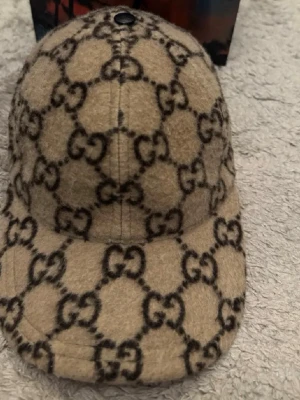 Beige GG-mönstrad keps från Gucci - Säljer en beige keps från Gucci med det klassiska GG-monogrammet i mörkbrunt över hela kepsen.  den är äkta som ni ser med kvitto och den är strl M och fraktar genom plick och den är jätte limited edition och nästan omöjligt o hitta i äkta den har inga skador eller något sånt 