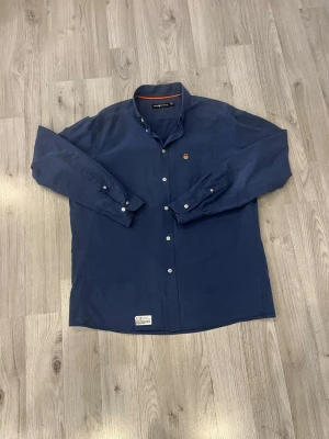 Sail racing skjorta  - Sail Racing skjorta  med klassisk button-down krage och vita knappar. Skjortan har en liten broderad logga på bröstet och etikett nertill. Tillverkad i mjuk bomull och har lång ärm. Perfekt för dig som gillar stilrena plagg med diskreta detaljer.