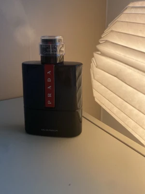 Prada Eau de Parfum OCEAN LUNA ROSSA - Snygg parfym från Prada i en elegant svart flaska med en röd vertikal etikett framtill. Flaskan har en modern, stilren design och ett silverfärgat sprayhuvud. Perfekt för dig som gillar exklusiva dofter och vill ha något lyxigt på hyllan.