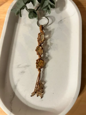 Makramé nyckelring med stenar - Handgjord makramé nyckelring med tre Citrin (trumlad)  stenar/kristaller,  i ljusbrunt snöre. Nyckelringen/Väsksmycke  har dekorativa” tofsar” glaspärlor i änden och en rostfri ring för enkel fastsättning. Perfekt accessoar för dig som gillar boho-stil och naturliga material. 💎