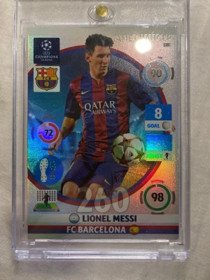 Panini Champions League Messi-kort - Säljer ett glittrigt samlarkort från Panini Champions League 2014-2015 med Lionel Messi i FC Barcelona. Kortet har holografisk yta, statistik och klubbmärke, samt är skyddat i plastfodral. Perfekt för dig som gillar fotboll och samlarkort.